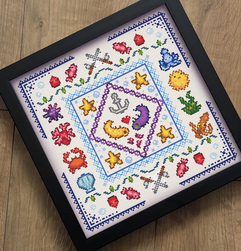 May include: Framed cross-stitch art featuring a nautical theme. The design includes an anchor, seahorse, starfish, and other sea creatures in various colors. The artwork is framed in a black square frame.