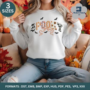 May include: A white long-sleeve sweatshirt featuring the word SPOOKY in large, patterned letters with a central peach-colored bow graphic. The design includes small black bat silhouettes scattered around the text. The sweatshirt has a crew neckline.