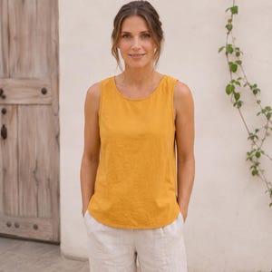 Puede incluir: Una camiseta sin mangas de color amarillo mostaza con cuello redondo y dobladillo recto. La prenda está confeccionada con una tela de color sólido y presenta un diseño sencillo y limpio con tirantes anchos y un ajuste relajado en el torso.