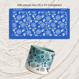May include: A blue silk screen stencil with a white rose pattern, measuring 22 x 11 centimeters, is displayed above a ceramic cup. The cup features a gradient of blue and white with a matching rose design.