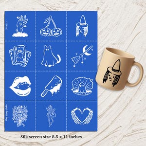 Puede incluir: Una pantalla de seda azul con ilustraciones blancas con temática de Halloween, que incluyen una bruja, naipes y un fantasma. Una taza beige con un diseño de bruja está a la derecha. La pantalla de seda mide 21,6 x 27,9 cm.