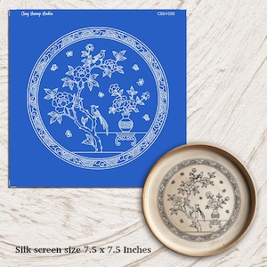 Könnte beinhalten: Ein blauer Siebdruck mit einem weißen Blumen- und Vogeldesign, neben einem Keramikteller mit dem gleichen Design. Der Siebdruck ist 19 x 19 cm groß. Das Design umfasst Blumen, Vögel und Schmetterlinge in einem kreisförmigen Rahmen.
