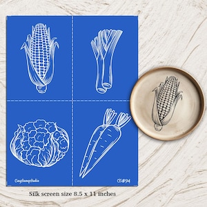Puede incluir: Una pantalla de seda azul con dibujos lineales blancos de verduras: maíz, puerros, coliflor y zanahorias. A la derecha, un plato de cerámica con un dibujo de maíz. El texto dice "Tamaño de la pantalla de seda 21,6 x 27,9 cm."