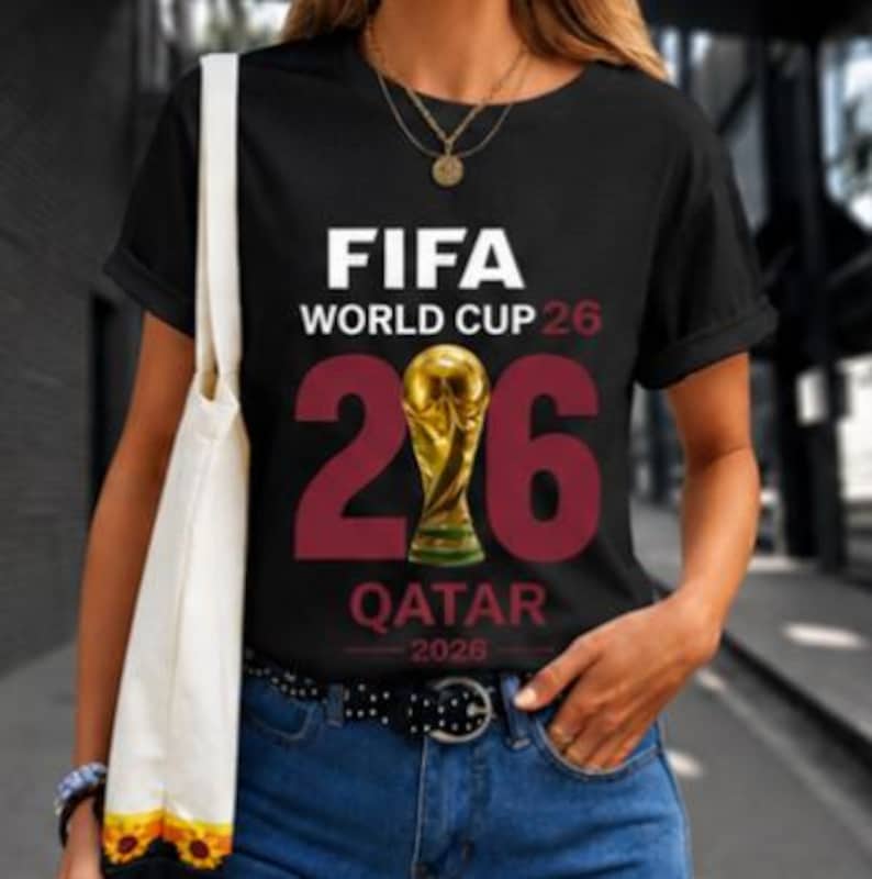 May include: Black t-shirt with the text "FIFA WORLD CUP 26" in white. The number "26" is in burgundy, with a gold trophy in the middle. Below the number is the word "QATAR" and the year "2026" in white.