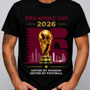 May include: Black t-shirt with the FIFA World Cup 2026 logo. The design features a gold trophy, a skyline silhouette, and the text "United by Passion, United by Football."
