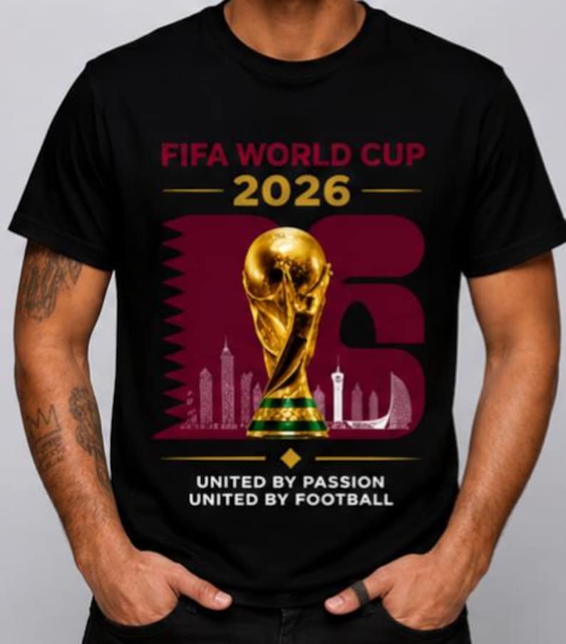 May include: Black t-shirt with the FIFA World Cup 2026 logo. The design features a gold trophy, a skyline silhouette, and the text "United by Passion, United by Football."
