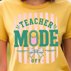 Puede incluir: Una camiseta color amarillo mostaza con un diseño gráfico de rayas verticales rosa claro. El texto TEACHER MODE OFF aparece en letras mayúsculas verde oscuro. Un lazo rosa claro está centrado bajo la palabra MODE, con dos puntos rosas junto a OFF.