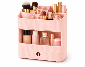 May include: A light pink plastic makeup organizer with a ribbed texture, featuring a top section with multiple compartments for brushes and lipsticks, and a lower open shelf containing various bottles, jars, and a small drawer with a circular handle.