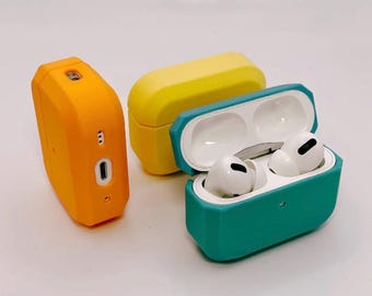 Op de afbeelding: Drie beschermende siliconen hoesjes voor draadloze oordopjes in oranje, geel en groenblauw. Het groenblauwe hoesje staat open en toont witte draadloze oordopjes. Elk hoesje heeft een geometrisch, gefacetteerd ontwerp met nauwkeurige uitsparingen.
