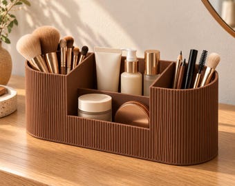 Op de afbeelding: Een bruine, ovale make-up organizer met een verticale geribbelde textuur. De houder heeft meerdere vakken met diverse cosmetische kwasten, een tube crème, een pompflacon, een klein potje en verschillende potloden.