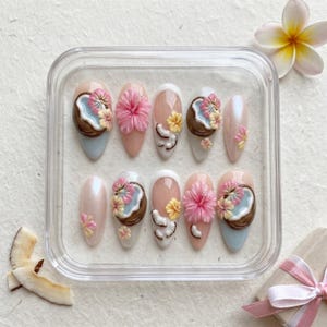 May include: A set of ten almond-shaped press-on nails arranged in a clear plastic container. The designs feature 3D sculpted pink hibiscus flowers, brown coconut halves with blue centers, and small yellow blossoms on nude, white, and pearlescent bases.