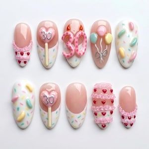 May include: A set of ten artificial nails with various designs. Some nails feature pink and white sprinkles, while others have heart-shaped decorations, a '30' design, and miniature balloons. The nails are oval-shaped and set against a white background.