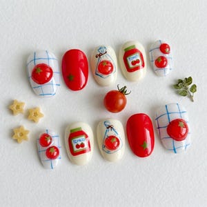 May include: A set of ten press-on nails featuring a tomato theme. Designs include solid red nails with small green stars, white nails with blue grid patterns and 3D red tomato accents, and white nails with illustrations of tomato jars and bags.