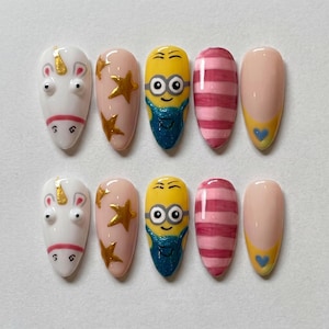 May include: A set of ten almond-shaped press-on nails. Designs include a white unicorn, pink nails with gold stars, yellow Minion characters, pink and red striped nails, and nude nails with a yellow tip and blue heart.