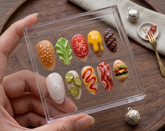 May include: A clear acrylic case holding ten uniquely designed nail art pieces, each resembling a component of a hamburger. The collection includes a bun, lettuce, tomato, cheese, a patty, onion, pickles, mustard, bacon, and a miniature burger.