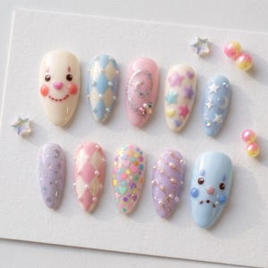 Puede incluir: Un juego de diez u&ntilde;as postizas en forma de almendra con varios dise&ntilde;os, incluyendo una cara de payaso, patrones de rombos azules y rosas con perlas, estrellas pastel, corazones, remolinos de purpurina y l&iacute;neas doradas con cuentas.