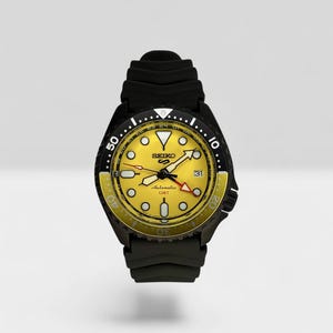 May include: A Seiko 5 Sports automatic GMT watch with a vibrant yellow dial, black rotating bezel with yellow accents, and a black silicone strap. The watch face features luminous markers, a date window, and the Seiko logo in black text.