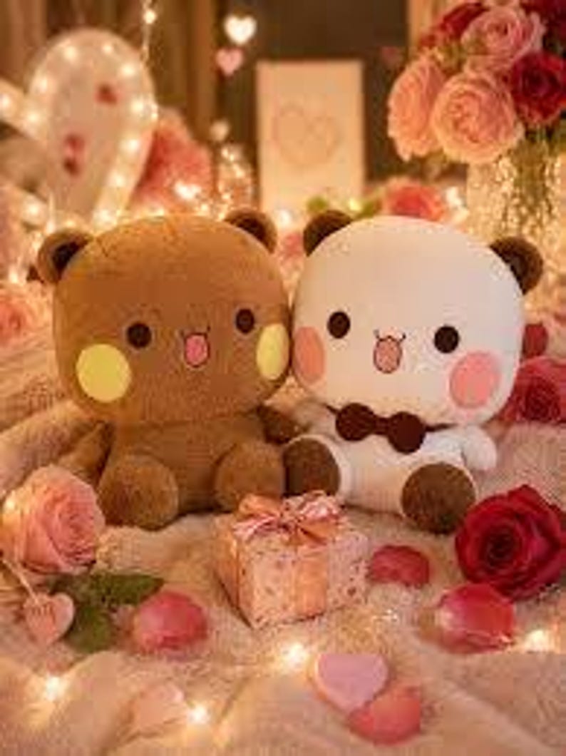 May include: Two plush bear toys, one brown and one white, with rosy cheeks and small tongues sticking out. A small gift box with a pink bow sits between them, surrounded by rose petals and fairy lights. The bears have brown ears and black eyes.