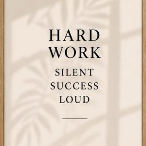 May include: A framed print with the words "HARD WORK SILENT SUCCESS LOUD" in black font. The print has a light beige background with a shadow of leaves. The frame is made of light brown wood.