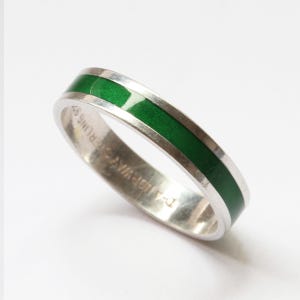 Könnte beinhalten: Ein Ring aus Sterlingsilber mit einer glatten, leuchtend grünen Emaille-Einlage, die entlang der Mitte der Außenfläche verläuft. Die Innenseite des Rings ist mit dem Text D-A NORWAY STERLING 925 graviert, was die Metallzusammensetzung angibt.