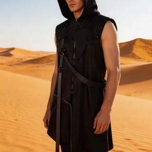 May include: A black sleeveless hooded vest featuring a front zipper closure, a high collar with decorative snap buttons, and an integrated harness-style strap system with metal rings that extends down the front of the garment.
