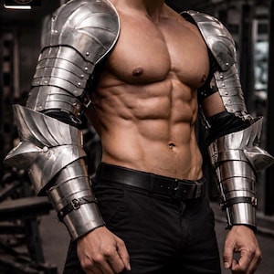 Puede incluir: Un conjunto de armadura de brazo de acero pulido que incluye hombreras articuladas y brazales a juego para los antebrazos. Las placas metálicas están aseguradas con correas de cuero oscuro y hebillas, con un diseño segmentado y coderas puntiagudas.