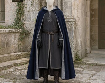 May include: A dark blue hooded cloak worn over a charcoal gray tunic with a silver circular emblem on the chest. The outfit includes a brown leather belt, black gloves, and dark brown boots. The cloak features a light gray lining.