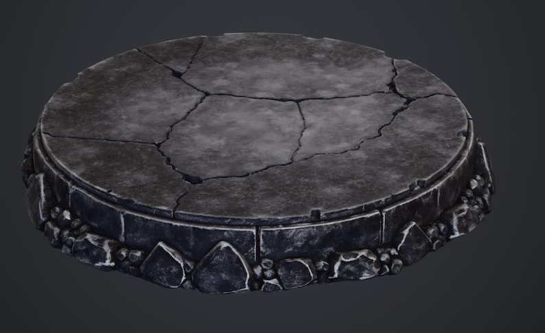 May include: A weathered, circular stone platform with a cracked surface. The platform has a dark gray color with a rough texture, and is surrounded by a border of stone blocks and small rocks. The platform is likely for display.