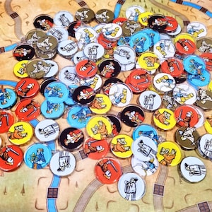 Op de afbeelding: Een verzameling ronde spelfiches met kleurrijke illustraties van middeleeuwse figuren, waaronder ridders, monniken en adel, verspreid over een bedrukt spelbordoppervlak met paden en terreindetails in verschillende tinten bruin en blauw.