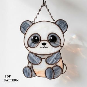 May include: Stained glass panda bear suncatcher with a chain for hanging. The panda has a white face and body with gray ears, arms, and legs. The eyes are large and black. The text "PDF PATTERN" is at the bottom.