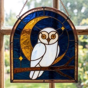 May include: A stained glass suncatcher featuring a white owl perched on a brown branch against a dark blue night sky. A large yellow crescent moon and small yellow stars are integrated into the design, all framed by a copper-colored metal border.