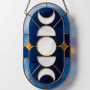 Può includere: Pannello in vetro colorato con un design celeste. Il pezzo di forma ovale presenta uno sfondo blu scuro con forme di luna crescente e cerchio bianche. Gli accenti includono scoppi di stelle dorate e un bordo azzurro. Una catena è attaccata per appenderlo. Il testo "PDF PATTERN" è in basso.