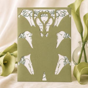 Könnte beinhalten: Eine rechteckige Klappkarte aus salbeigrünem Karton mit aufwendigen Laserschnitten in Form von Calla-Lilien. Die Karte gibt den Blick auf eine weiße Einladungskarte frei, die mit dunkelgrünen botanischen Linienzeichnungen bedruckt ist.