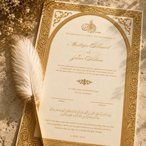 May include: A rectangular marriage certificate with an ornate gold border, featuring the names Mustafa Ahmed and Sana Aslam, dated April 2026. A white feather quill pen with a gold tip rests on the document, which includes English and Arabic text.