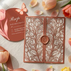 K&ouml;nnte beinhalten: Eine terrakottafarbene RSVP-Karte mit Tulpenillustration und Schmetterlingsgrafik, kombiniert mit einer lasergeschnittenen Klappkarte mit Tulpenmuster und einem runden Wachssiegel, umgeben von frischen pfirsich- und orangefarbenen Tulpen.