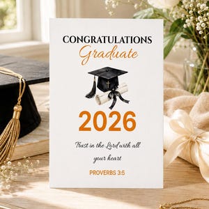 May include: A 5x7 inches graduation greeting card featuring the text CONGRATULATIONS Graduate 2026, a black graduation cap with a cross, a diploma, and the scripture Trust in the Lord with all your heart PROVERBS 3:5 in black and orange.