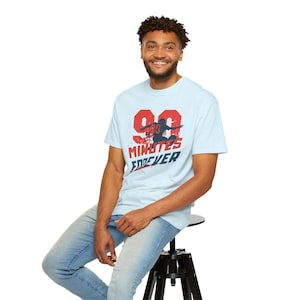 Puede incluir: Camiseta azul claro con un gráfico desgastado. El gráfico incluye el número "99" en rojo, una silueta de jugador de fútbol americano y las palabras "Minutes Forever" en rojo y azul. La camiseta la lleva una persona.