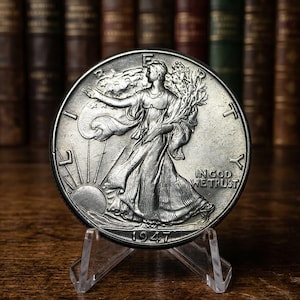 May include: A silver Walking Liberty half dollar coin from 1947, displayed on a clear acrylic stand. The coin features Lady Liberty walking towards the sun, holding branches. The words "IN GOD WE TRUST" are visible.