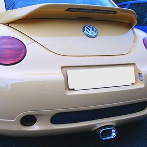 Può includere: Una Volkswagen Beetle giallo pallido vista dal retro. L'auto presenta una carrozzeria arrotondata, uno spoiler posteriore con luce di stop integrata, luci posteriori rosse circolari, un emblema Volkswagen centrale e un singolo tubo di scarico cromato.