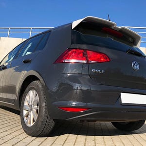 Könnte beinhalten: Ein dunkelgrauer Volkswagen Golf Schrägheck von hinten in der Dreiviertelansicht. Das Fahrzeug verfügt über einen weißen Heckspoiler, rote Rückleuchten, silberne Leichtmetallfelgen und den Schriftzug GOLF in silbernen Buchstaben am Kofferraum.