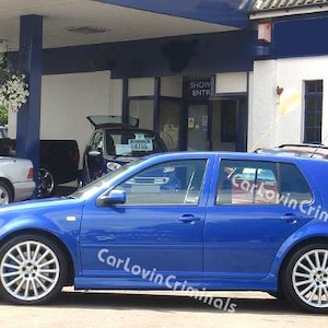Könnte beinhalten: Ein leuchtend blaues Schrägheckauto auf einem Parkplatz in Seitenansicht mit silbernen Mehrspeichen-Leichtmetallfelgen. Der Text CarLovinCriminals ist über die Karosserie des Fahrzeugs gelegt, das vor einem Gebäude mit blauen Verzierungen steht.