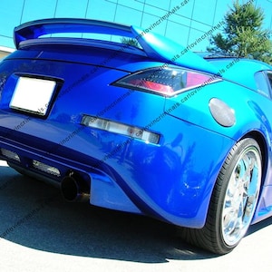 Pode incluir: Um carro esportivo azul brilhante visto de um ângulo traseiro, com um grande aerofólio, escapamento duplo, lanternas traseiras transparentes, uma tampa de combustível prateada e rodas cromadas de raios. O carro tem uma placa branca vazia.