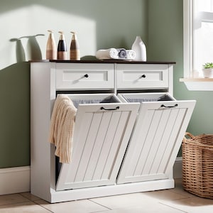 May include: A white wooden laundry hamper cabinet with a dark brown top surface, featuring two top drawers with black knobs and two tilt-out compartments with black handles. A cream-colored textured blanket hangs over the left compartment door.