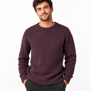 May include: A dark plum-coloured long-sleeve jumper featuring a thick, textured crochet knit pattern, a rounded crew neckline, and ribbed cuffs and hem. The garment is constructed with a dense, uniform stitch throughout the body and sleeves.