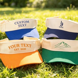Pode incluir: Quatro viseiras com faixas na cor creme e abas coloridas em azul, azul marinho, laranja e verde. As viseiras apresentam texto bordado incluindo CUSTOM TEXT, NAME, YOUR TEXT EXT. 2026 e um gráfico de montanha em linhas verdes na frente.