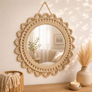 May include: A round, woven mirror with a scalloped edge hangs on a white wall. The mirror is made of natural-colored fibers and has a leather strap for hanging. The mirror reflects a room with neutral tones and natural light.