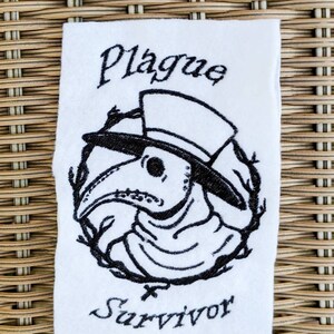 May include: Black and white embroidered patch with a plague doctor wearing a hat and mask. The text "Plague Survivor" is embroidered below the image.