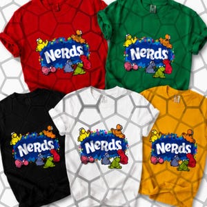 May include: Five short-sleeved crew neck t-shirts in red, green, black, white, and yellow. Each shirt features a central graphic with the word "NERDS" in white letters against a blue splash, surrounded by small colourful cartoon characters.