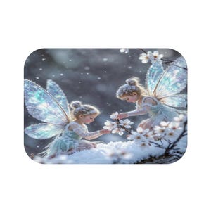 Puede incluir: Dos pequeñas figuras con alas iridiscentes y translúcidas están arrodilladas en la nieve blanca. Visten ropa de colores claros con textura y extienden sus manos hacia una rama cubierta de pequeñas flores blancas mientras caen copos de nieve.