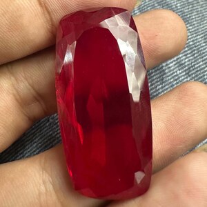 May include: A large, rectangular, faceted gemstone with a deep, vibrant red colour. The stone features a polished surface with multiple geometric facets that reflect light, creating a brilliant, translucent appearance throughout the entire piece.